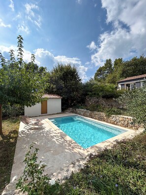 A rectangular swimming pool with a stone wall surrounding it, a small shed, and a garden area with various plants and a bench. - New Listing (Fayence)
