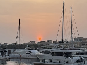 A marina with multiple yachts docked, a sunset in the background, and residential buildings in the distance. - Luxury 3BD Apartment in Palm Jumeirah | Marina Views & Stunning Sunsets (Dubai)
