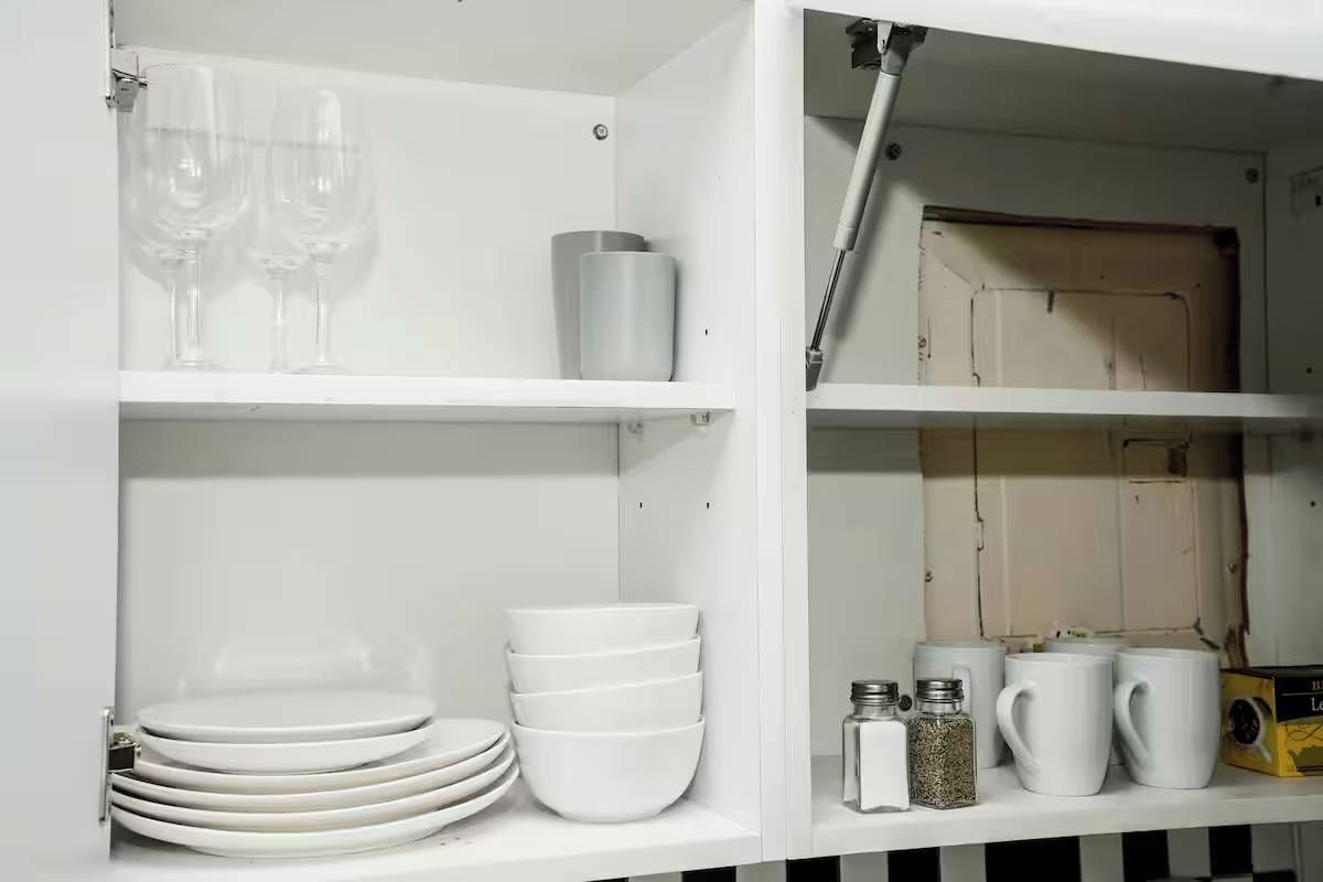 A white cabinet with shelves holding plates, bowls, glasses, and a box.