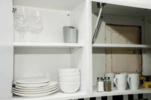 A white cabinet with shelves holding plates, bowls, glasses, and a box. - Lexington studio (New York)