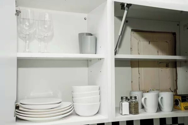 A white cabinet with shelves holding plates, bowls, glasses, and a box. - Lexington studio (New York)