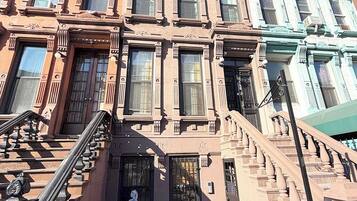 A row of brownstone buildings with a central staircase leading to the entrance.