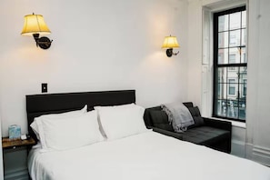 A hotel room with a bed, bedside tables, lamps, and a window with a view. - Lexington studio (New York)