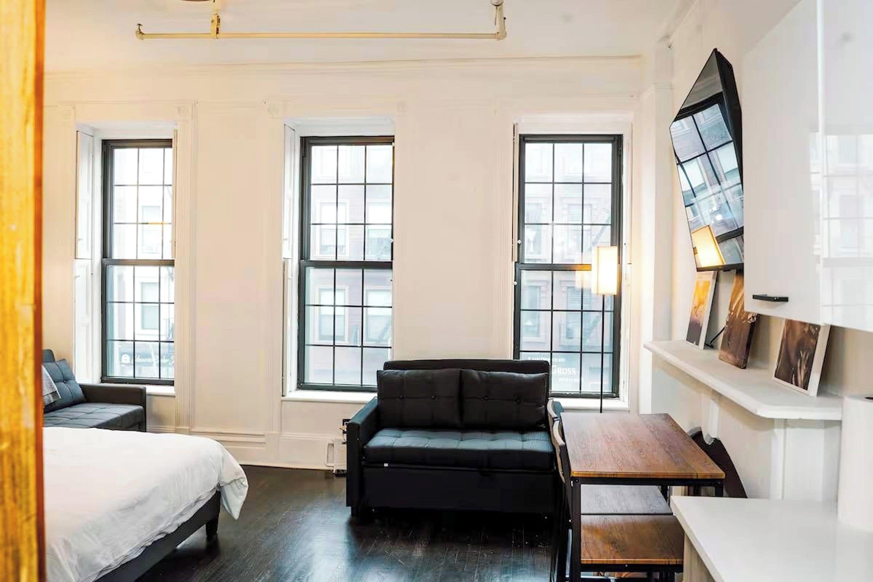 A room with a bed, a sofa, a desk, and three windows.