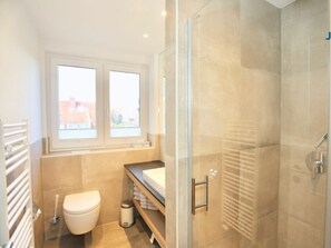 A modern bathroom with a glass shower enclosure, a toilet, a sink, and a window providing natural light. - 213 - Apartment 13 "red Crab" (Juist)