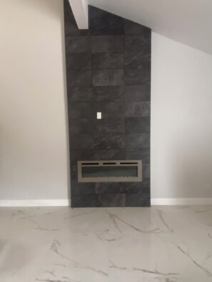 Um quarto com parede de azulejos escuros, lareira embutida e chão de mármore.