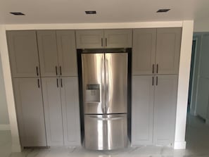 Un frigorifero in acciaio inox in una cucina con mobili grigi e pareti bianche.