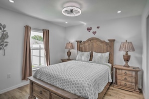 A bedroom with a bed, bedside tables, lamps, a window with curtains, a ceiling light, and decorative heart-shaped wall art. - Sun 'n Lake Kozy Korner - Private Hot Tub & Pets Welcome (Sebring)