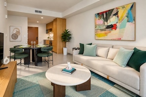 A modern living room with a sofa, a coffee table, and a dining area with chairs and a table set for two. - Miami Skyline Suite | Balcony, Rooftop Pool & Gym (Miami)