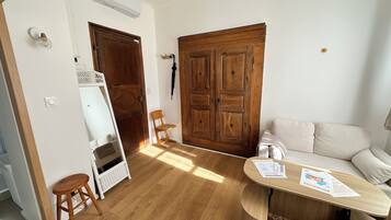 Una habitación con piso de madera, un sofá blanco, una silla de madera, un armario blanco y una puerta grande de madera.