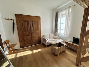 Une pièce comprenant une armoire en bois, un canapé, une petite table avec des papiers, un téléviseur et une fenêtre avec des rideaux.