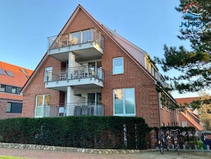 A two-story brick building with a balcony on the upper floor, a stone wall in front, and bicycles parked outside. - 211 - Apartment 11 "sandkornchen" (Juist)