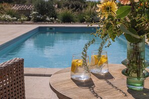 Ein Poolbereich mit einem Holztisch, zwei Gläsern mit klarer Flüssigkeit und Zitronenscheiben sowie einem grünen Blumentopf mit Grünpflanzen.
