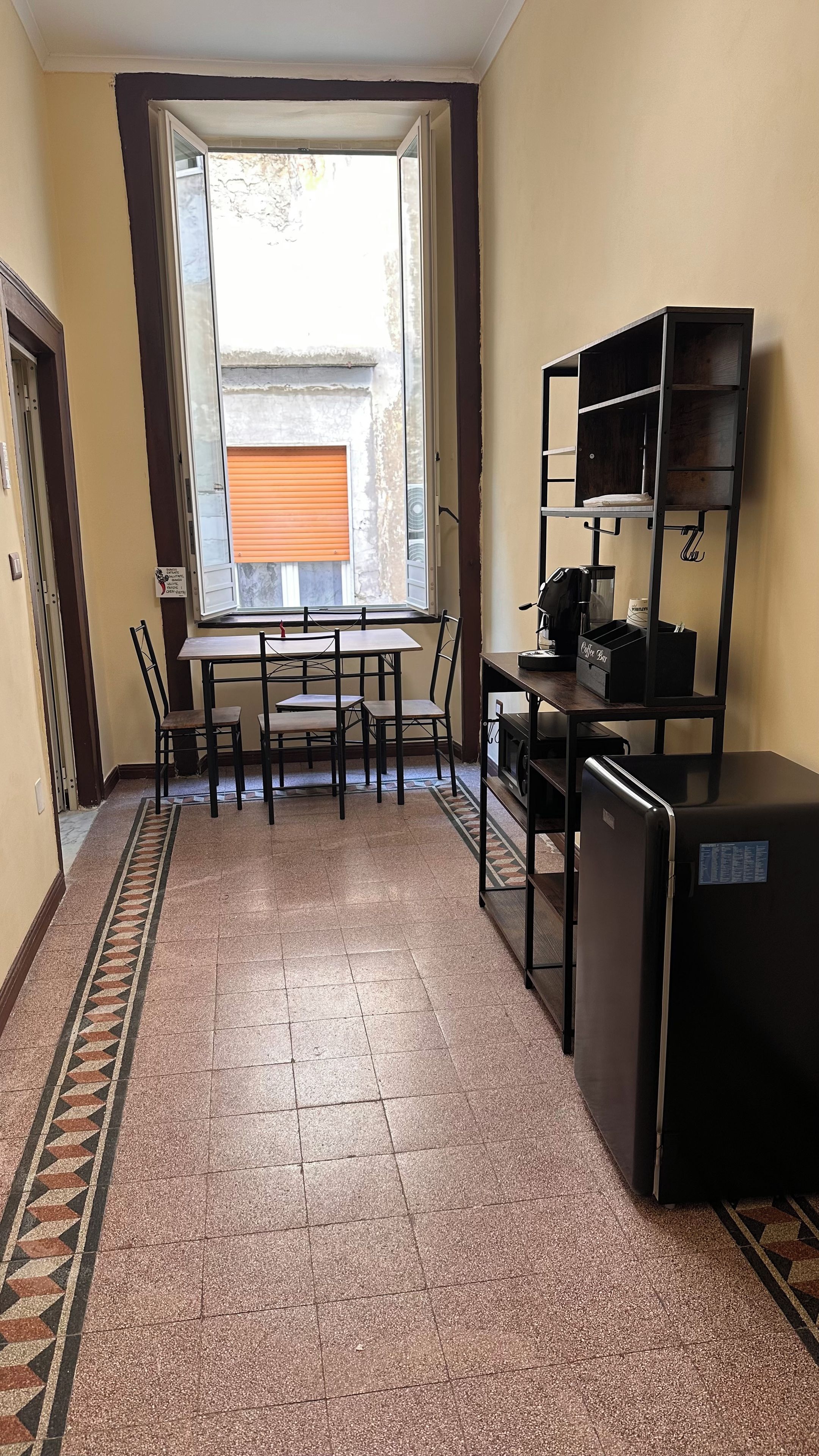 A small kitchenette with a refrigerator, a sink, and a countertop. There is a window with a view of the outside.
