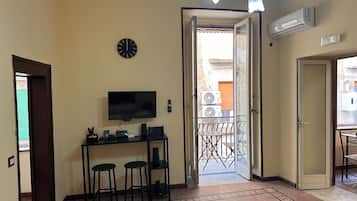 A room with a TV, a clock, and a door leading to a balcony with outdoor furniture.