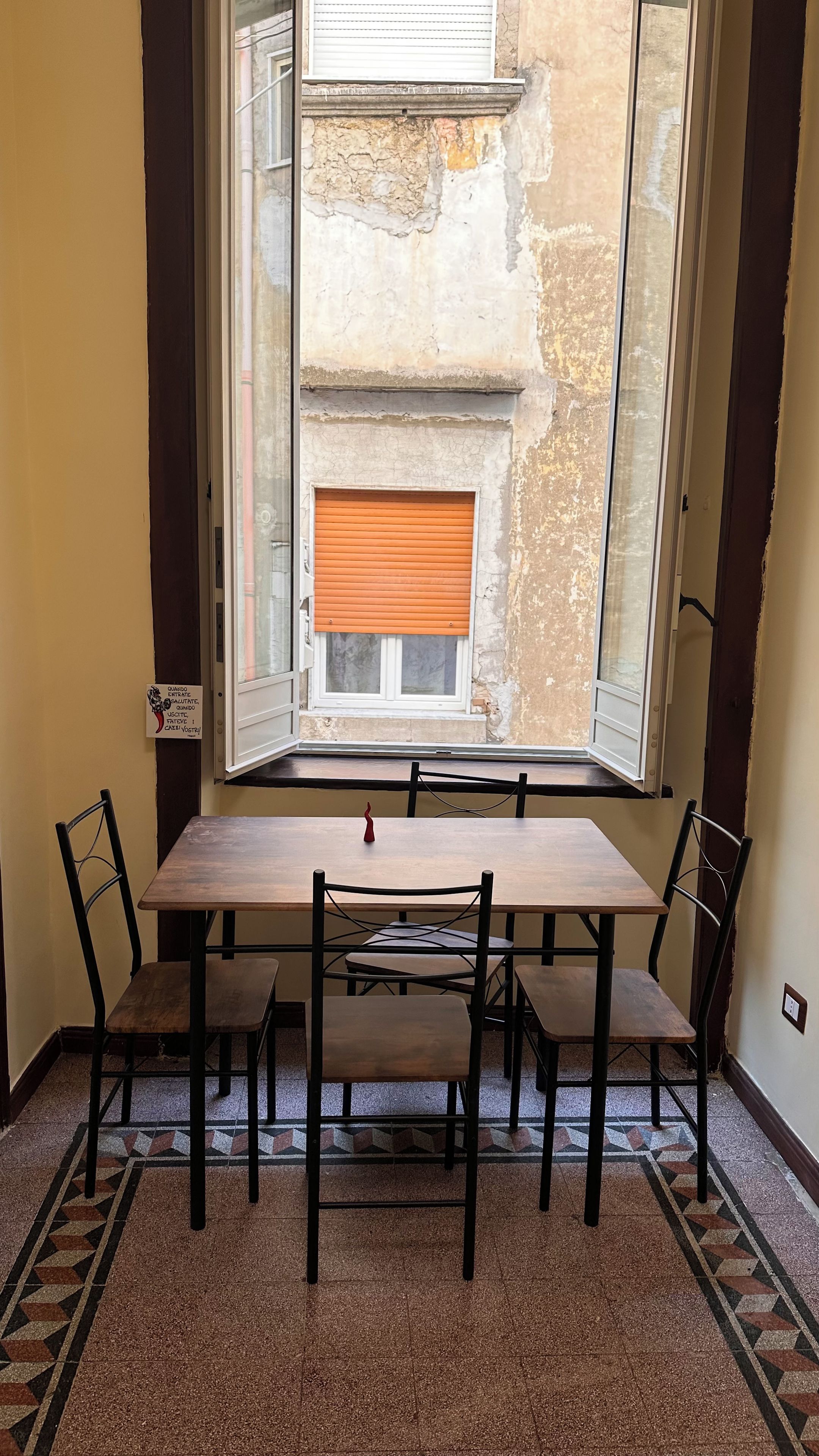 A dining area with a table and chairs, a window with a view of a building, and a patterned floor.