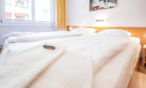 A hotel room with two beds, a window with curtains, a wall-mounted light, and a framed picture. - ELEGANT 2-BEDROOM APARTMENT WITH FIREPLACE & MOUNTAIN VIEWS (Zermatt)