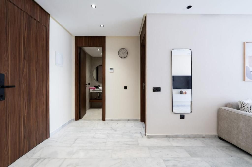 A hallway with a wooden wardrobe, a mirror, a clock, and a sofa.