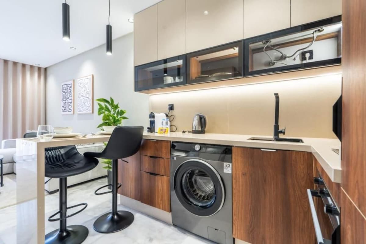 Een moderne keuken met een ingebouwde wasmachine, een koffiezetapparaat en een eethoek met barstoelen.