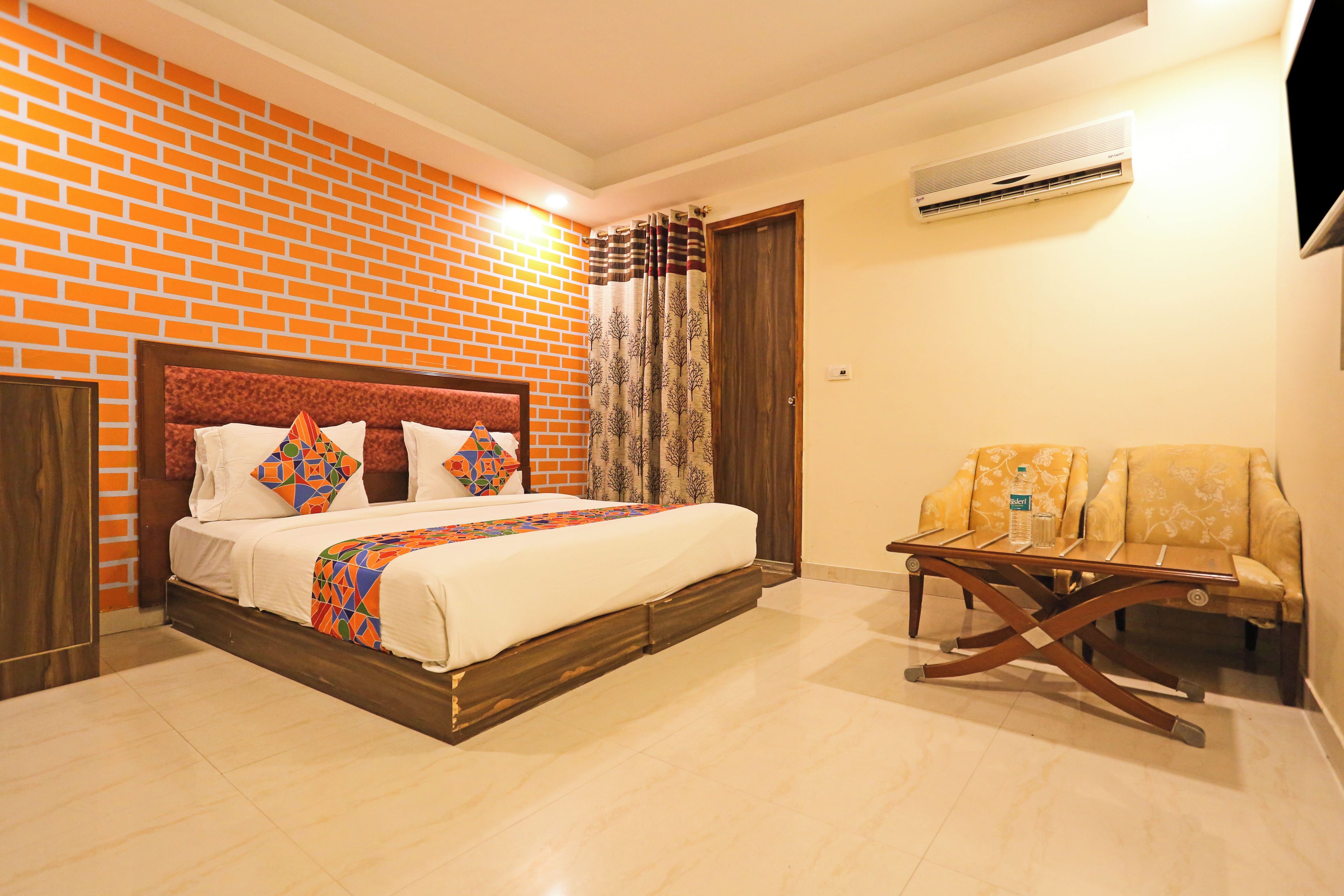 Habitación de hotel con pared de ladrillo, cama con cabecera de madera, una pequeña mesa con sillas y un equipo de aire acondicionado en la pared.