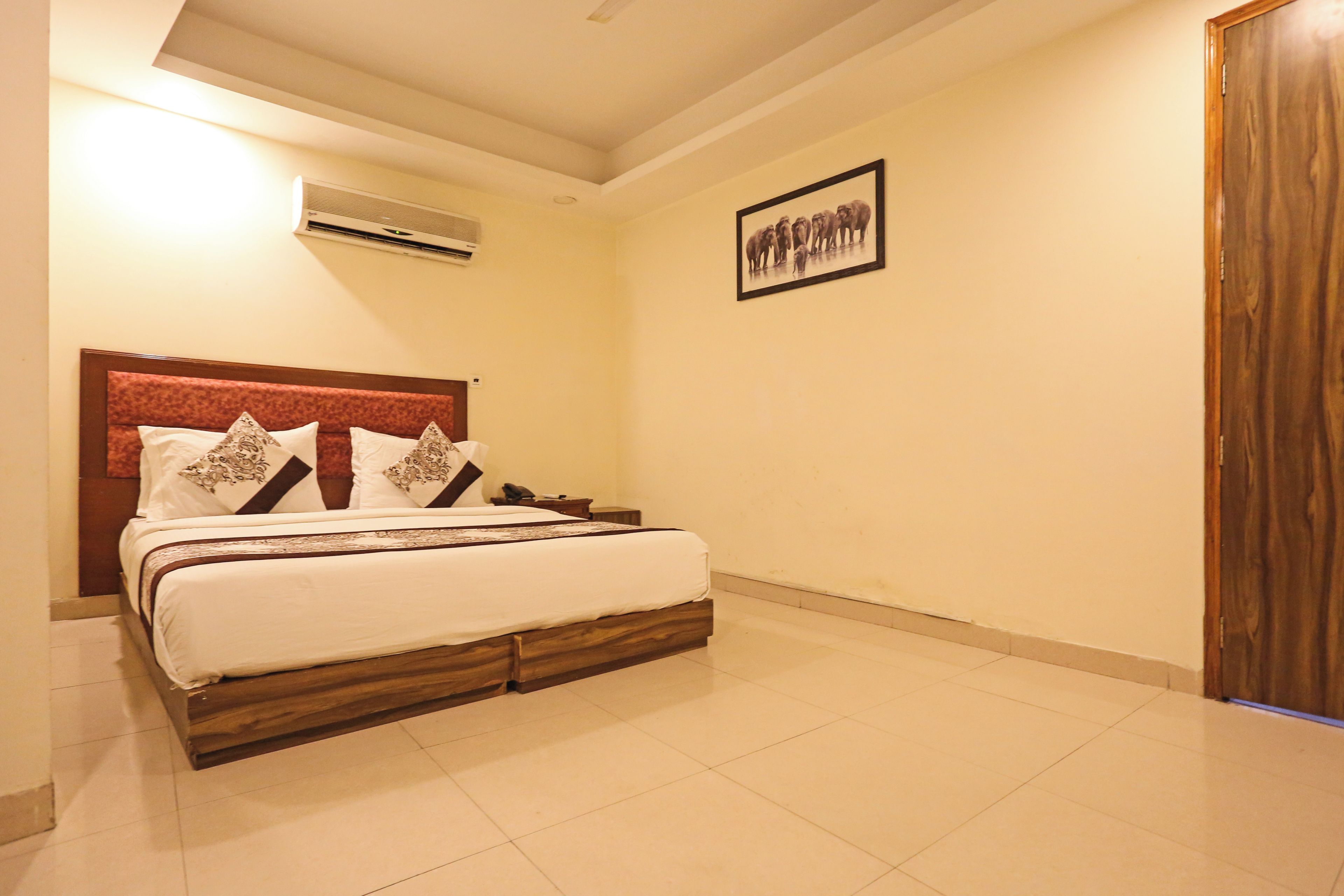 Una habitación de hotel con una cama, una mesita de noche, aire acondicionado de pared y un cuadro enmarcado.