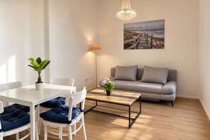 A modern living room with a white table, blue cushioned chairs, a grey sofa, a wooden coffee table, and a floor lamp. - Vienna Days and Cozy Nights 1BR with Lounge near Westbahnhof (Vienna)