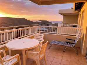 A balcony with a round table and chairs, a striped lounge chair, and a view of the ocean at sunset. - Clube Praia da Rocha Apartments by Agsuites (Portimão)