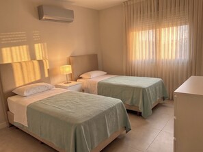 A hotel room with two beds, a nightstand with a lamp, and a window with sheer curtains. - Clube Praia da Rocha Apartments by Agsuites (Portimão)