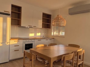 Uma cozinha moderna com armários brancos, forno embutido e uma área de refeições com mesa e cadeiras de madeira.