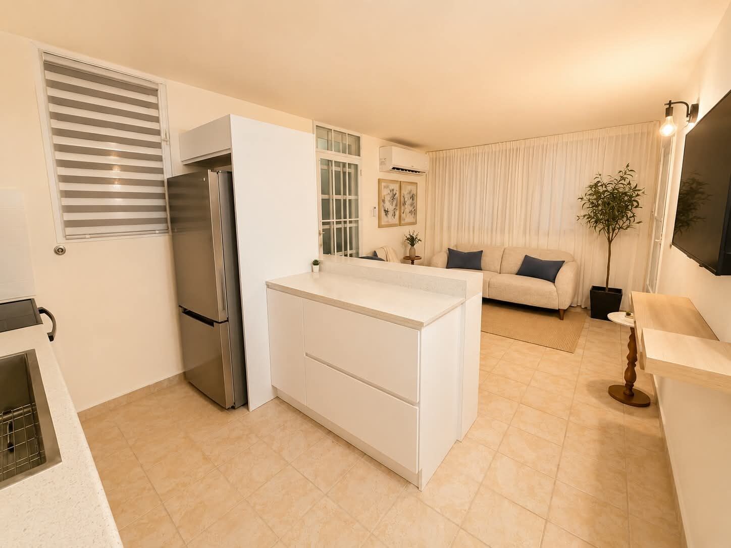 Una cocina compacta con refrigerador incorporado, un área de comedor con sofá y una planta en maceta.