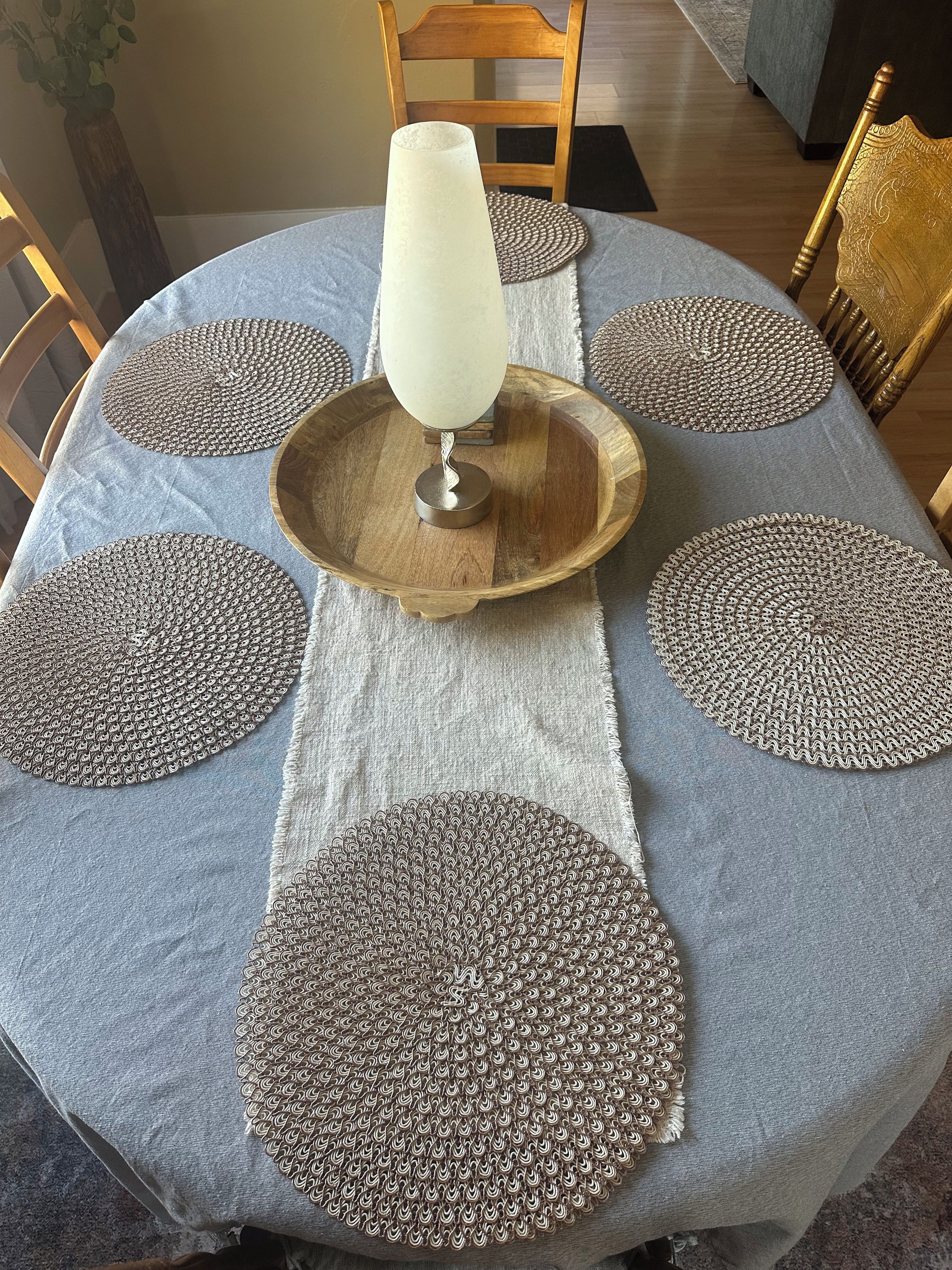 A round table with a white tablecloth, a wooden tray, and decorative coasters.
