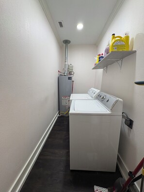 Une buanderie équipée d’un lave-linge et d’un sèche-linge, d’un chauffe-eau et d’une étagère contenant des produits de nettoyage.