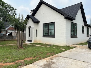 Une maison de plain-pied à l’extérieur blanc, avec des bordures noires, une porte de garage bien visible et une allée menant à une voiture garée.