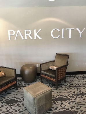 Ein Sitzbereich mit einem 'PARK CITY' Schild, einem gemusterten Teppich und einem runden Hocker.
