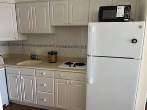 A kitchen with white cabinets, a microwave, a stove, and a refrigerator. - Cozy 1-bedroom condo in pleasant Daytona Beach with AC and gym (Daytona Beach)