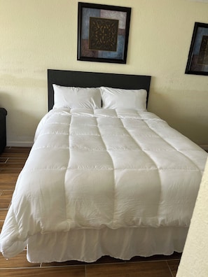 A bed with a white duvet, a dark headboard, and a framed picture on the wall. - Cozy 1-bedroom condo in pleasant Daytona Beach with AC and gym (Daytona Beach)