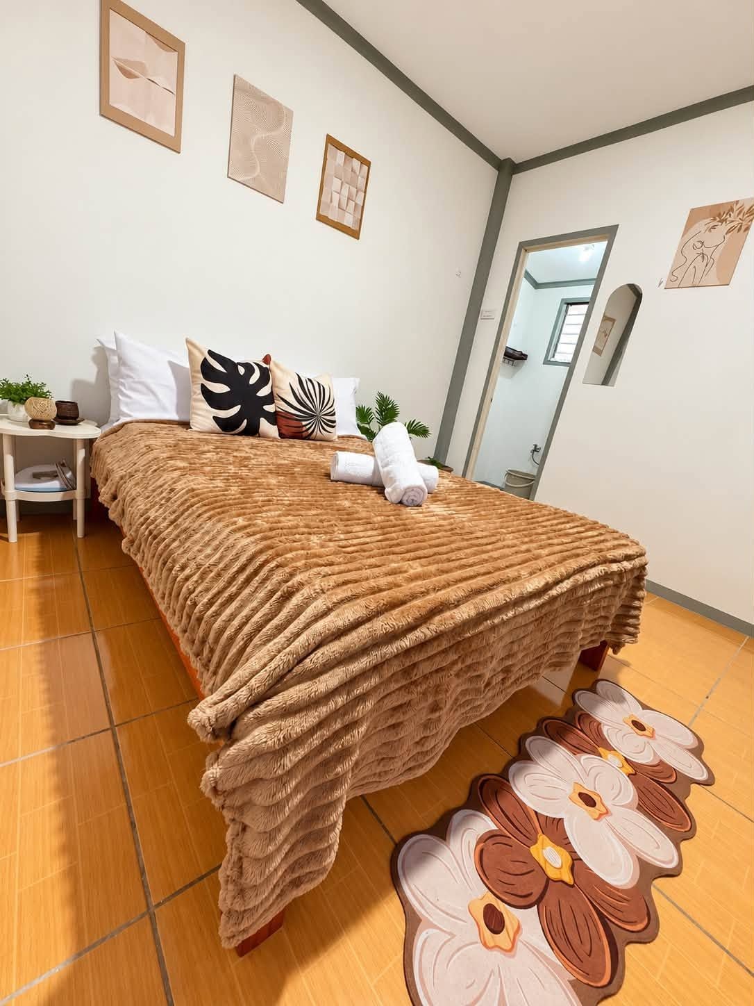 A neatly made bed with a textured blanket, a small bedside table with a plant, and a mirror on the wall.