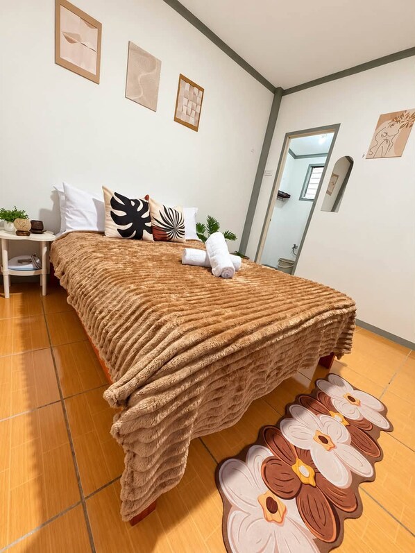 A neatly made bed with a textured blanket, a small bedside table with a plant, and a mirror on the wall. - Lovely 1-bedroom house in Moalboal perfect for a relaxing getaway (Moalboal)