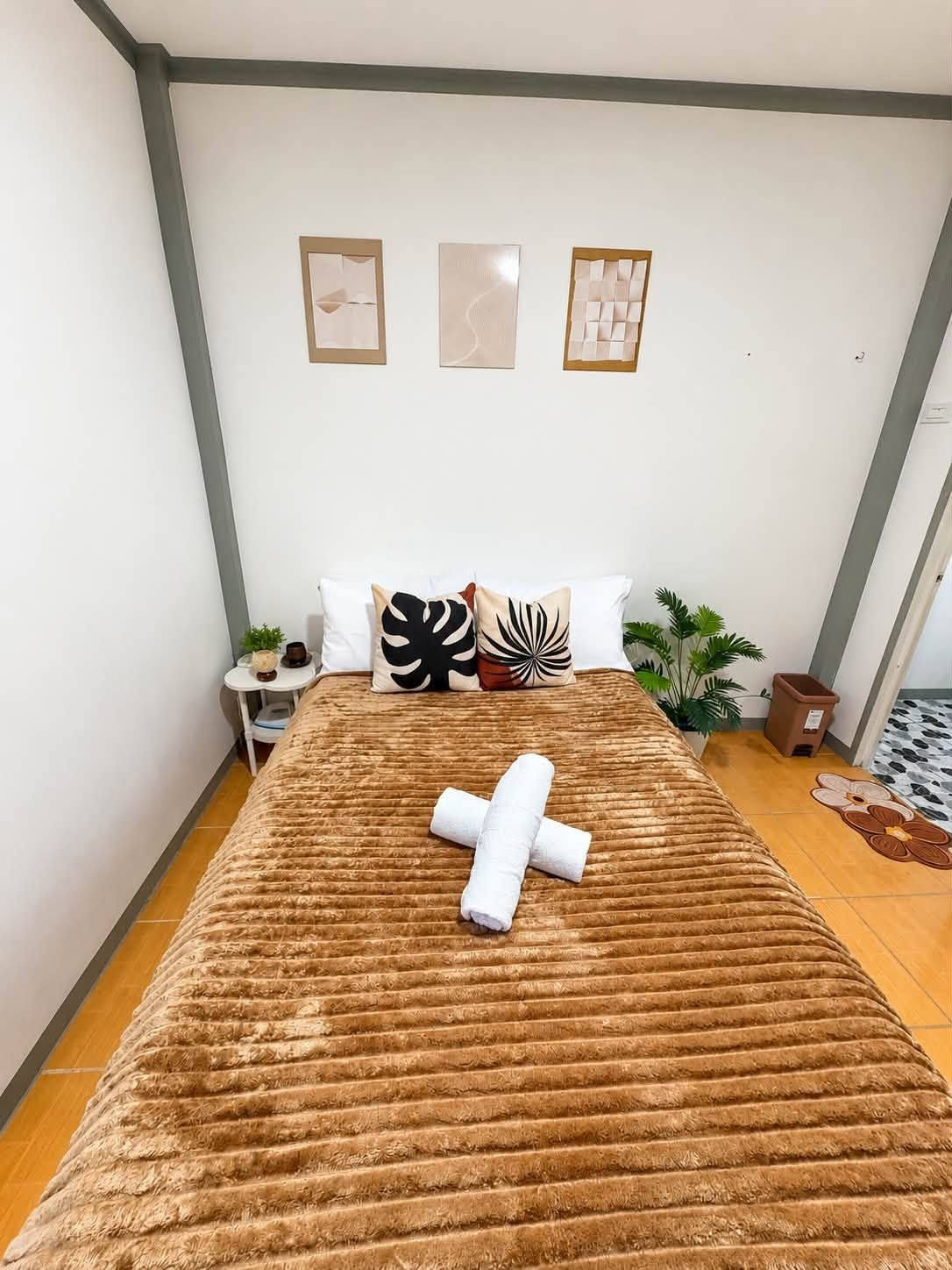 A bedroom with a large bed, a small bedside table, a potted plant, and artwork on the wall.