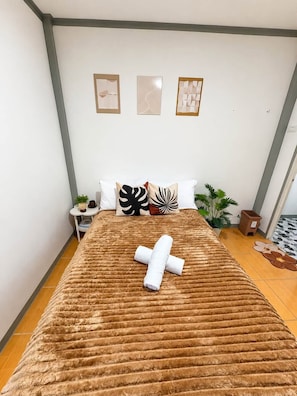 A bedroom with a large bed, a small bedside table, a potted plant, and artwork on the wall. - Lovely 1-bedroom house in Moalboal perfect for a relaxing getaway (Moalboal)