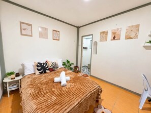 A bedroom with a bed, pillows, a bedside table, a mirror, and artwork on the walls. - Lovely 1-bedroom house in Moalboal perfect for a relaxing getaway (Moalboal)