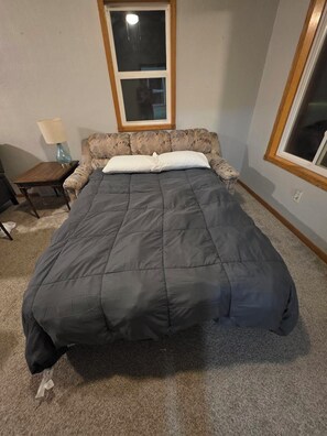 Quarto com cama, mesa de cabeceira, abajur e janela.