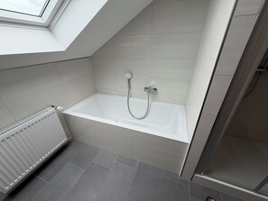 Une salle de bain moderne avec une baignoire, une douche et une fenêtre de toit.