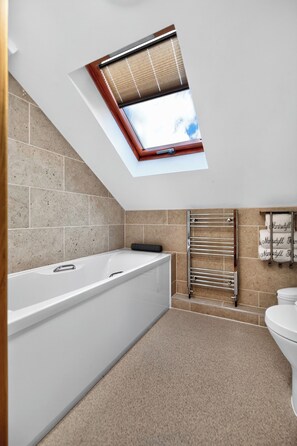 Een moderne badkamer met dakraam, bad, toilet en handdoekhouder.