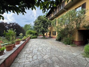 Ein Innenhof mit Pflasterung, Kübelpflanzen und einem Gebäude mit Balkonen.