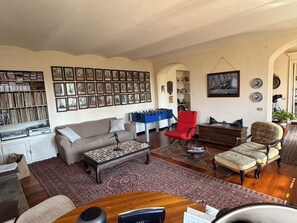 Ein Wohnzimmer mit einer Couch, Sesseln, einem Couchtisch, einem Bücherregal und einem Kicker.