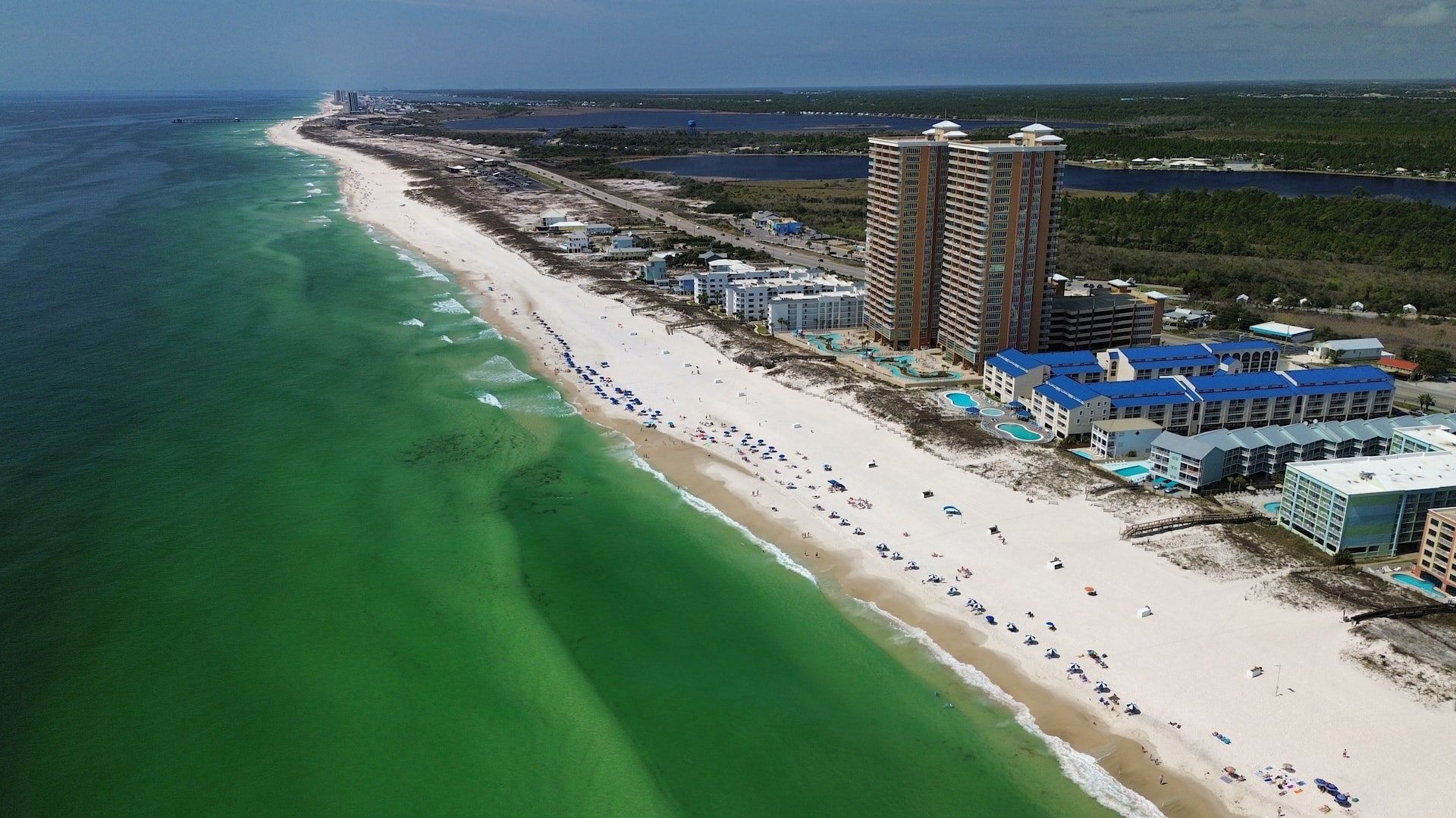 A coastal resort with a long sandy beach, multiple high-rise buildings, and a clear view of the ocean.