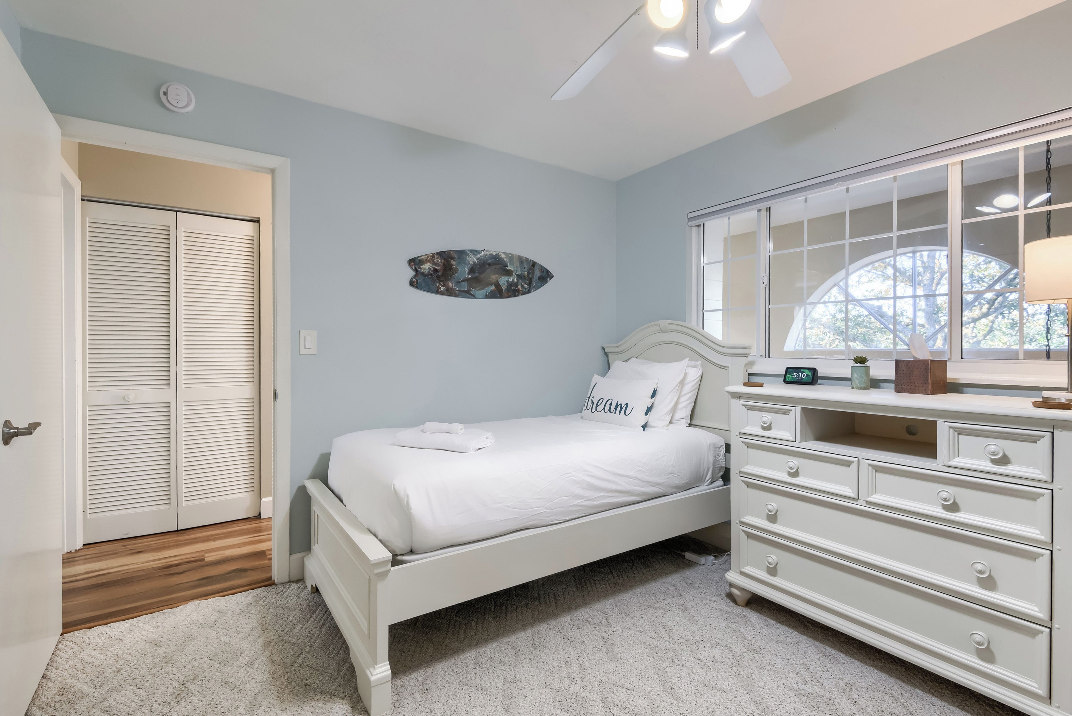 Une chambre à coucher avec un lit, une commode, un miroir, une horloge et une fenêtre.