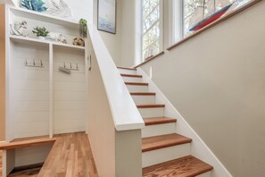 Eine Treppe mit Holzstufen und weißen Wänden, die zu einer Empfangshalle mit Kleiderständer und Ablagefläche für Dekorationen führt.