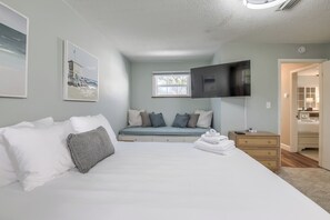 Een slaapkamer met een bed, een bankje, een televisie en een zichtbare badkamer door een open deur.